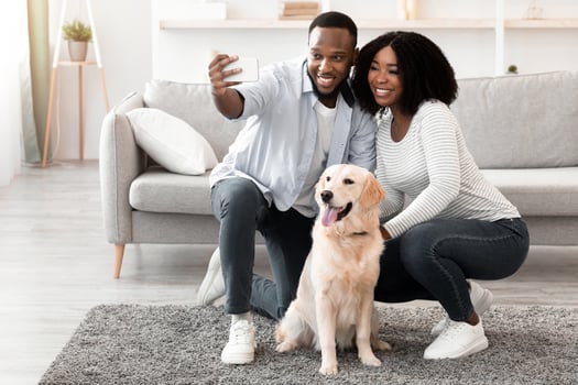 Happy Loving Family. Portrait of adult black couple taking selfie with their dog in living room, sitting on the floor at home. Man using smartphone for photo, spending time with domestic animal photo