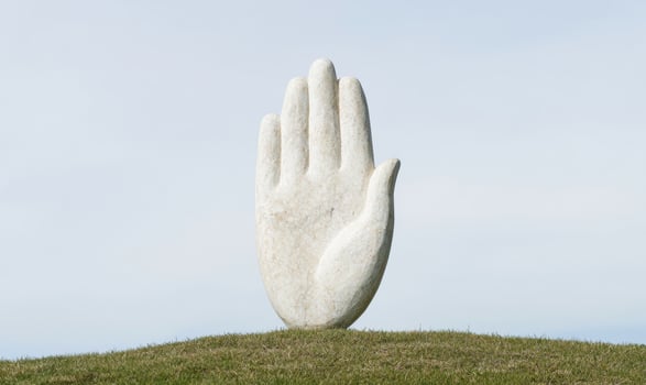 large hand sculpture on grassy hill against clear sky photo