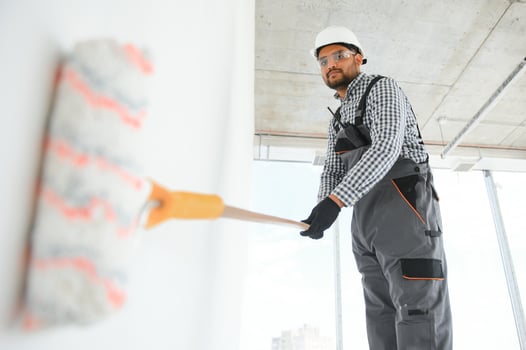 An Indian apartment repair worker paints a white wall with a roller photo