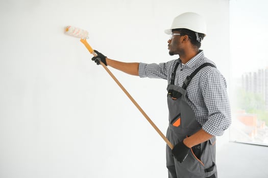 African man paints a white wall with a roller. Repair of the interior photo