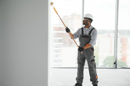 African man paints a white wall with a roller. Repair of the interior photo