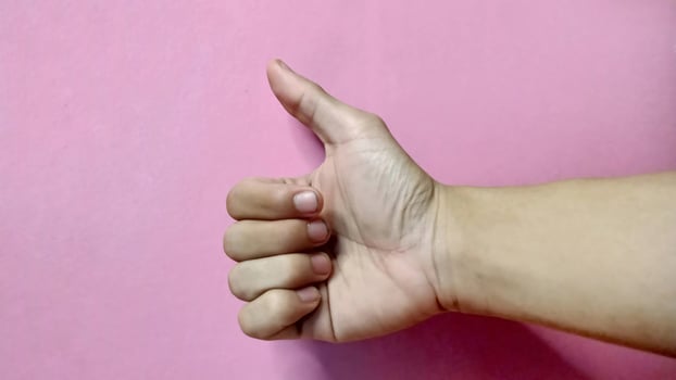 Close up of hand gesturing thumbs up against a pink backdrop. Positive, approval, success concept. photo