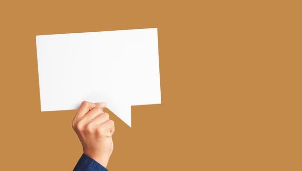 Close-up of hand holding a white speech bubble against a light brown background photo