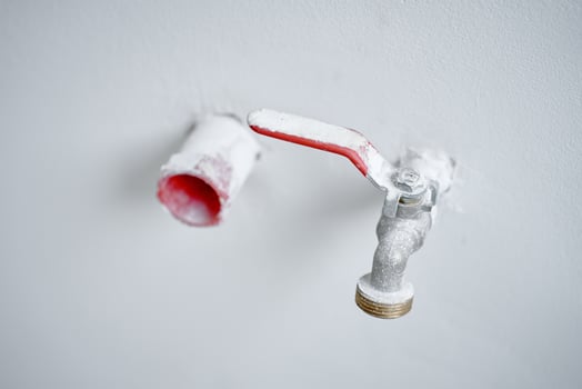 Close-up of water faucet with red handle protruding from white wall in empty apartment. Plumbing work during home renovation photo