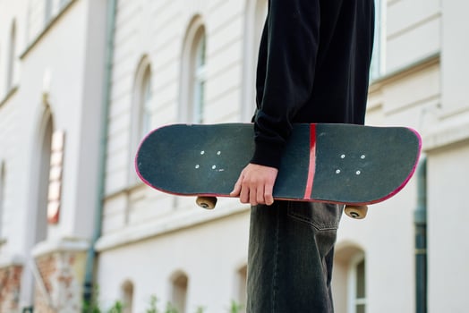 Skateboarder in baggy jeans holding scratched skateboard walking at city street. Teenager is skateboarding. Concept of youth subculture photo