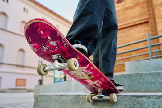 Skateboarder balancing on pink skateboard. Close-up of teenager feet wearing jeans and black sneakers skateboarding at street stairs. Leisure activity and extreme sport concept photo