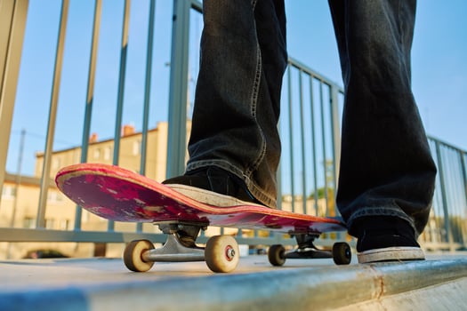 Skateboarder balancing on scratched pink skateboard at skatepark. Close-up of teenager feet wearing jeans and black sneakers skateboarding at skatepark. Leisure activity and extreme sport concept photo