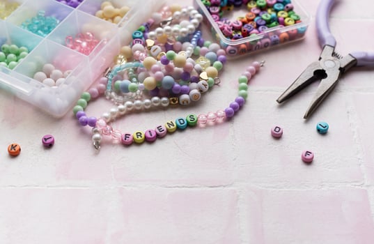 Colorful beads and pliers arranged on pink tile for jewelry making photo
