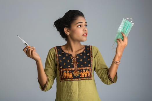 young woman holding a medical mask and thermometer. medical thermometer to illustrate protection from viruses, flu and respiratory diseases. photo