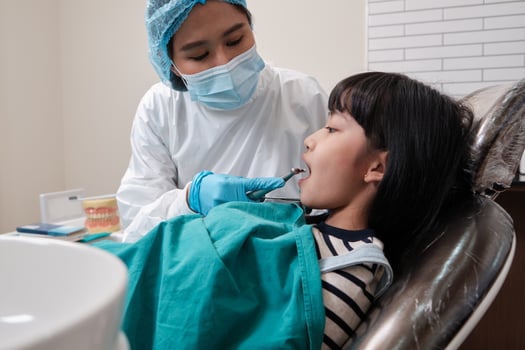 Asian female pediatric dentist checks and examines a little Thai girl's caries teeth in dental clinic, well-being mouth oral hygiene, and professional orthodontic healthcare work in a kid hospital. photo