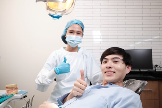 Portrait of Asian female dentist and male patient thumbs up, tooth whitening implant, happy smile, and looking at camera in dental clinic, mouth hygiene healthcare work in a doctor's hospital. photo