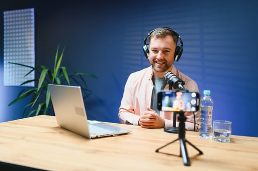 Man podcaster influencer blogger smiling while broadcasting his live audio podcast in studio using headphones. Male radio host making podcast or interview photo