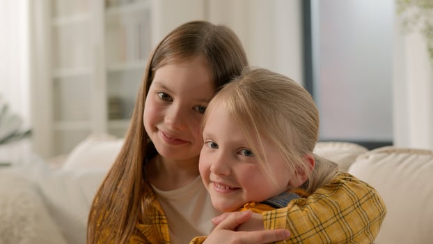 Portrait happy cute little caucasian girls children sisters kids friends smiling look at each other hugging embracing cuddle looking camera family love care affection relationship embrace hug indoors photo