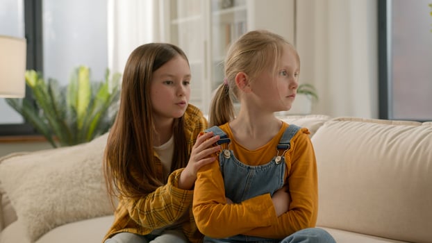 Two little Caucasian kids children siblings daughters girls argument remorseful sister apologizing hugging asking forgiveness younger sister ignoring feel offended angry family quarrel couch indoors photo