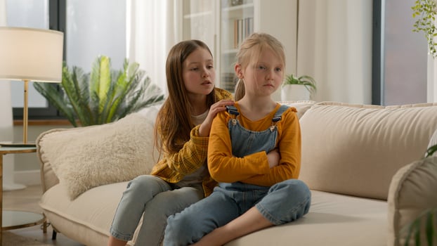 Two little Caucasian kids children siblings daughters girls argument remorseful sister apologizing hugging asking forgiveness younger sister ignoring feel offended angry family quarrel couch indoors photo