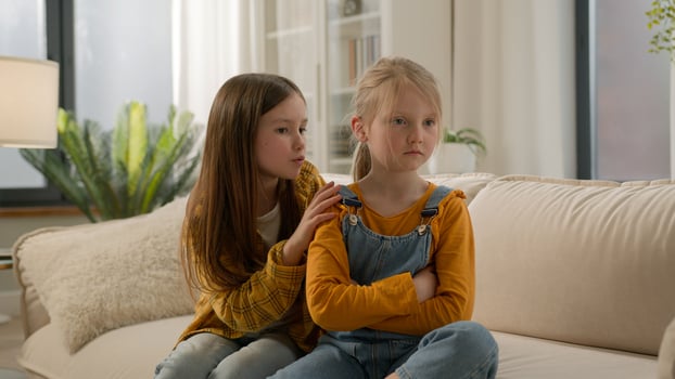 Two little Caucasian kids children siblings daughters girls argument remorseful sister apologizing hugging asking forgiveness younger sister ignoring feel offended angry family quarrel couch indoors photo