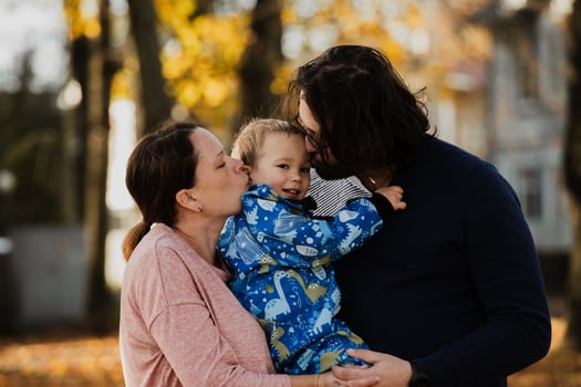 On a sunny autumn day in the park, a mother and father lovingly embrace their young son, sharing moments of laughter and joy as they play together photo