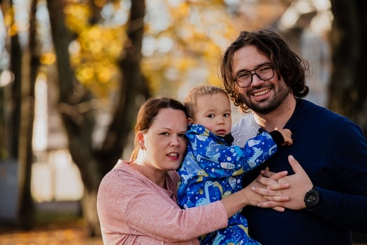 On a sunny autumn day in the park, a mother and father lovingly embrace their young son, sharing moments of laughter and joy as they play together photo
