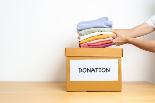 Donation, Charity, Volunteer, Giving and Delivery Concept. Hand holding Clothes into Donation box at home or office for support and help poor, refugee and homeless people. Copy space for text photo