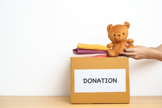 Kid Donation, Charity, Volunteer, Giving and Delivery Concept. Hand holding Bear doll and Clothes into Donation box at home for support and help poor, refugee and homeless people. Copy space for text photo