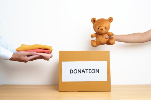 Kid Donation, Charity, Volunteer, Giving and Delivery Concept. Hand holding Bear doll and Clothes into Donation box at home for support and help poor, refugee and homeless people. Copy space for text photo