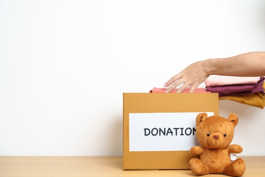 Kid Donation, Charity, Volunteer, Giving and Delivery Concept. Hand holding Bear doll and Clothes into Donation box at home for support and help poor, refugee and homeless people. Copy space for text photo