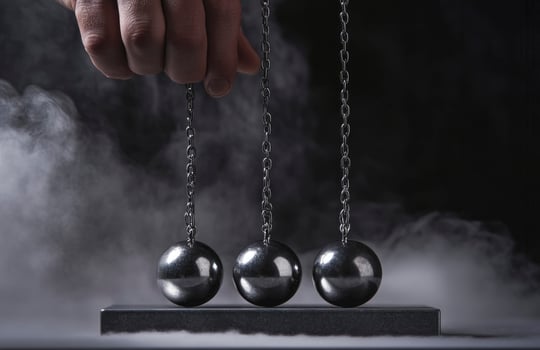 A hand is holding three balls that are suspended by chains. The balls are silver and appear to be in motion. photo
