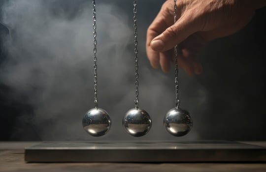 A hand is holding three balls that are suspended by chains. The balls are silver and appear to be in motion. photo