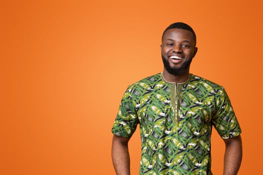 Confident black man in green african costume posing over yellow studio background photo