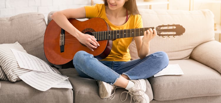 Stay home, have fun. Pretty musical girl with notes playing acoustic guitar on comfy sofa indoors photo