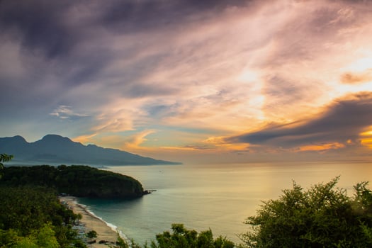 Virgin Beach in Karangasem, Bali, in the morning as seen from atop a cliff. The view features dramatic clouds at sunrise with green hills below photo