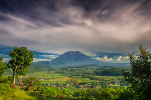 Mount Agung and Bug Bug village are visible from the top of the hill, along with the expanse of rice fields surrounding the village under a dramatic morning sky photo