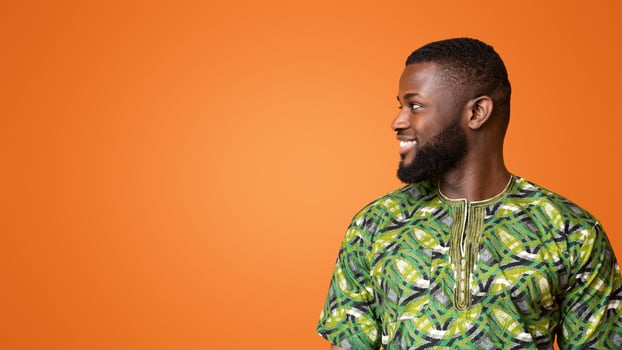 Interested african man in traditional costume looking at copy space over yellow background, panorama photo