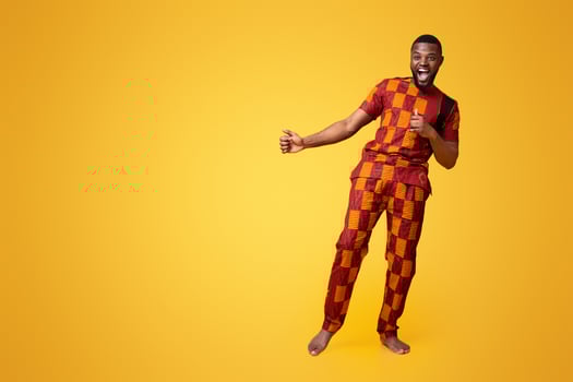 Funny african guy in traditional clothes laughing over yellow studio background photo