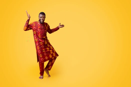 Positive african man in traditional dress dancing over yellow studio background photo
