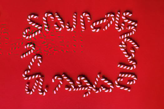 Flat lay Christmas composition with frame of candy canes on a red background. photo
