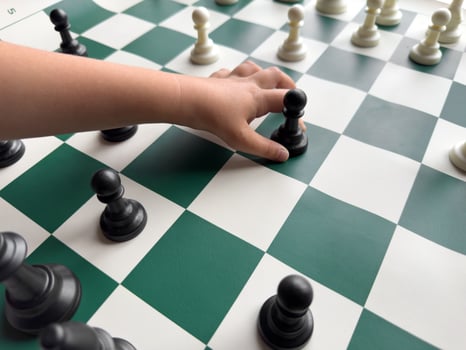 Childs hand holding chess pawn on green and white chessboard photo
