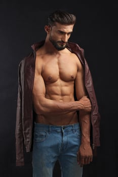 portrait of a young pakistani gym fit male model showing his build physique bicep triceps arms shoulder wings along with brown jacket photo