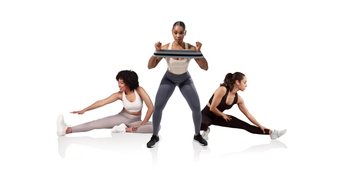 Three women participate in a fitness session, with one performing squats while holding a weight and the others stretching. The modern studio environment is bright and motivational. photo