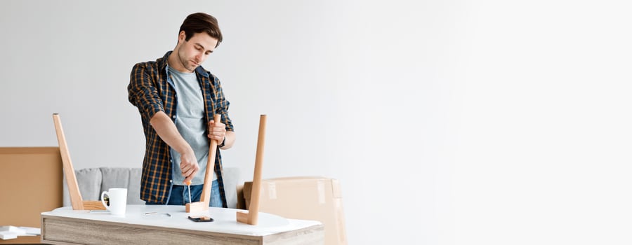 Work, new purchase, assembly and fix furniture at home. Concentrated millennial man screwing detail with screwdriver at carpenter workplace with tools and cup in living room interior, copy space photo