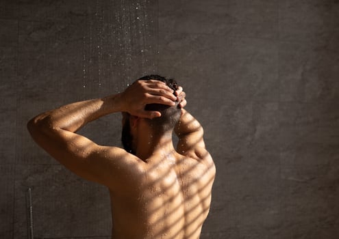 Back Rear View Of Adult Muscular Man Taking Shower Washing Head Standing Under Falling Hot Water In Modern Bathroom At Home. Male Bodycare Beauty Routine And Everyday Hygiene Concept photo