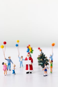 Miniature Santa Claus holding a gift surrounded by children and colorful balloons photo
