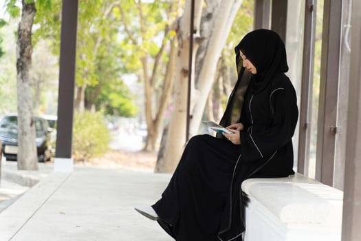 Side view of Muslim student wearing abaya niqab traditional clothes sit relaxing with tablet in university with sun fare and blurred background. photo