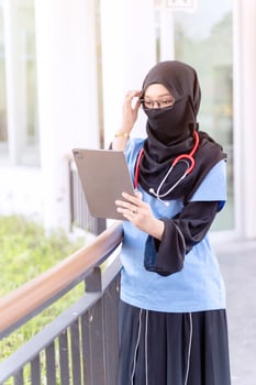 Female Muslim doctor in Abaya niqab traditional clothes works and check list on tablet at modern clinic office with sun fare background. photo