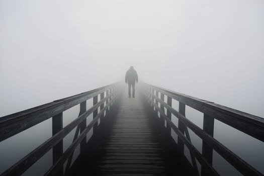 Solitary figure stands at the end of a narrow wooden bridge in thick fog photo
