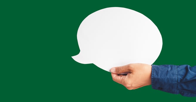 Close-up of hand holding a white speech bubble against a green background photo