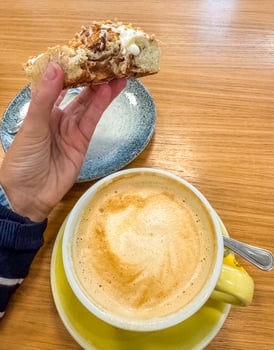 female hand holding bitten bun and yellow cup of coffee on wooden table . High quality photo