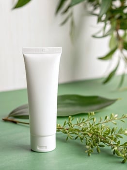 White cosmetic tube with green leaves on a sage green background. photo