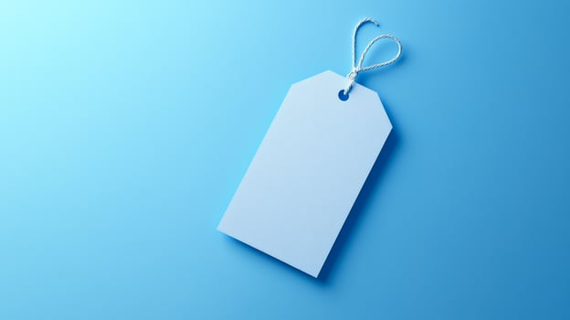 A blank blue tag rests on a smooth light blue surface, ideal for labeling or pricing items artistically. photo