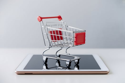 Mini shopping cart rests on tablet screen, metallic frame against white background photo